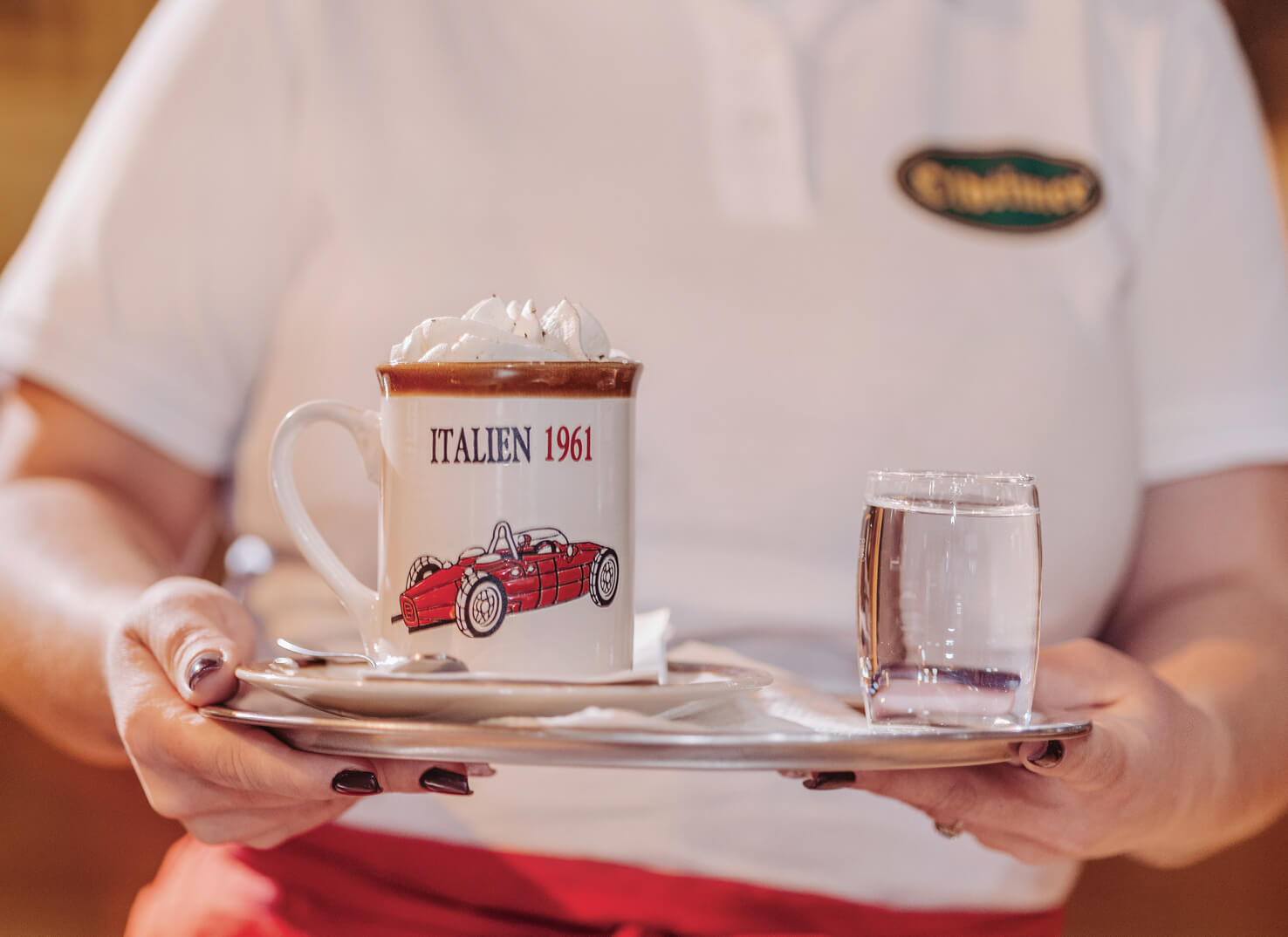 Ein Häferlkaffe mit Schlagobers wird im Oldtimer Häferl mit einem Glas Wasser am Tablett serviert.